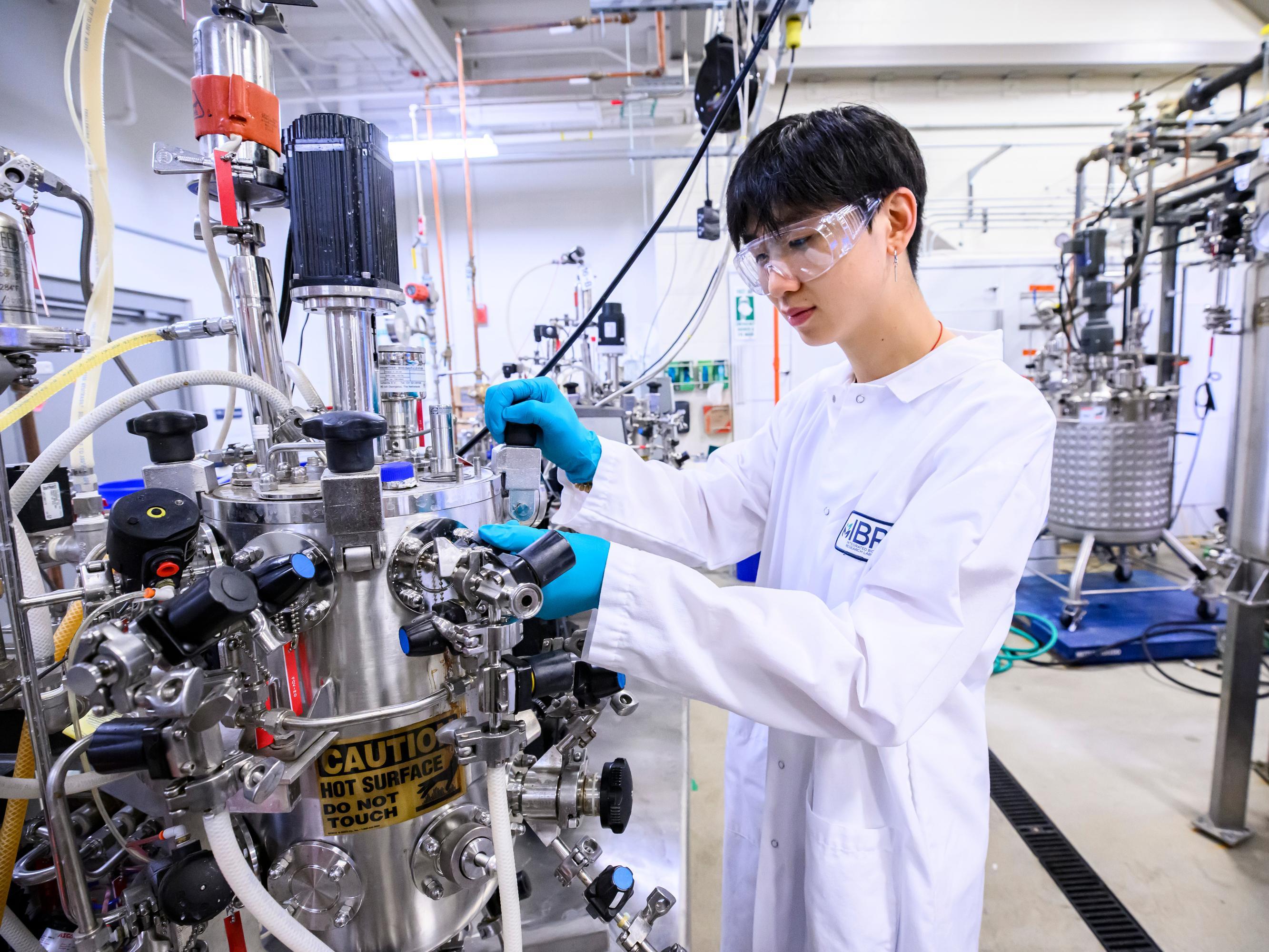 An IBRL researcher in a lab coat interacts with lab equipment.