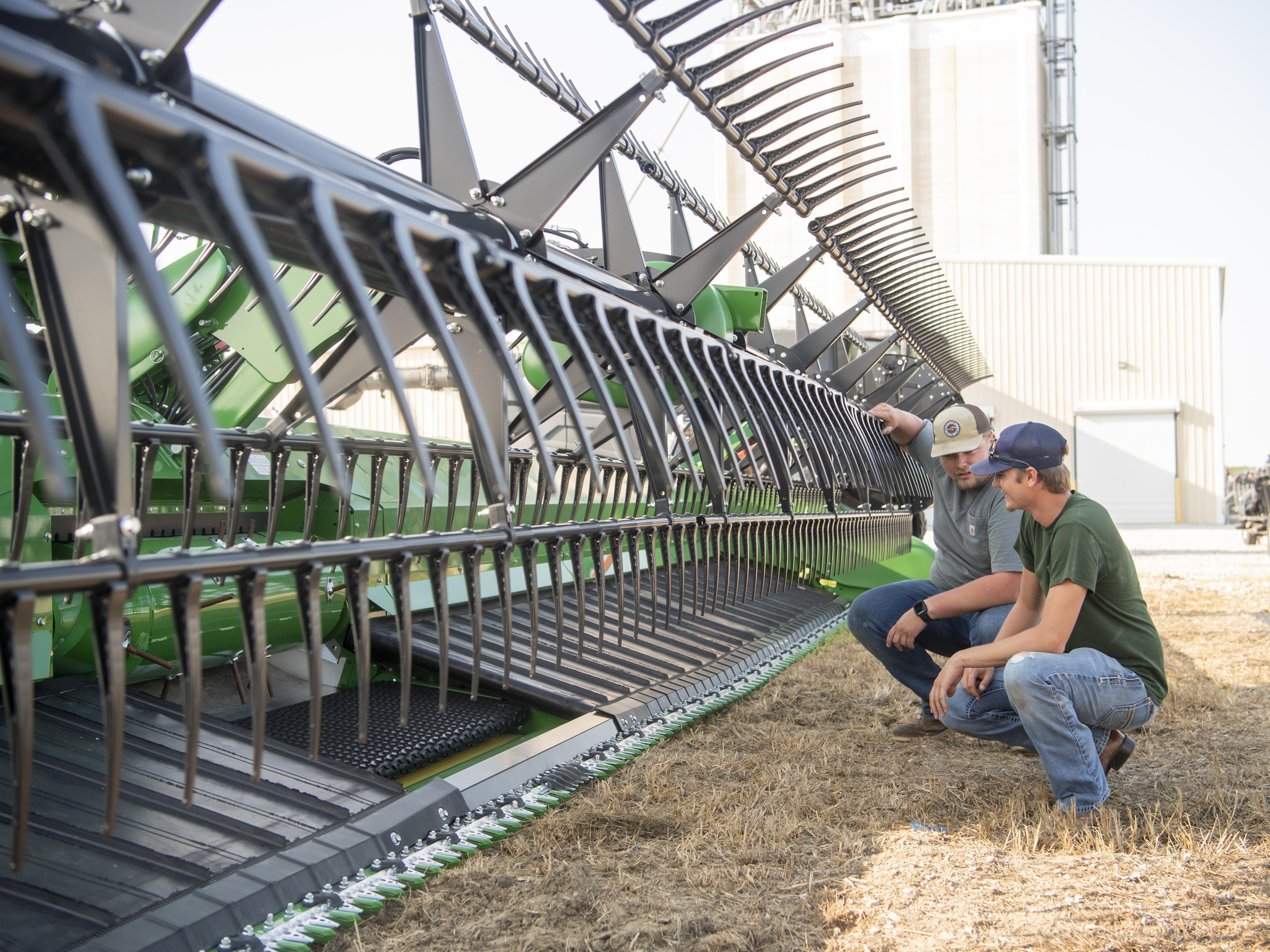 Two men crouching by a large tractor component.