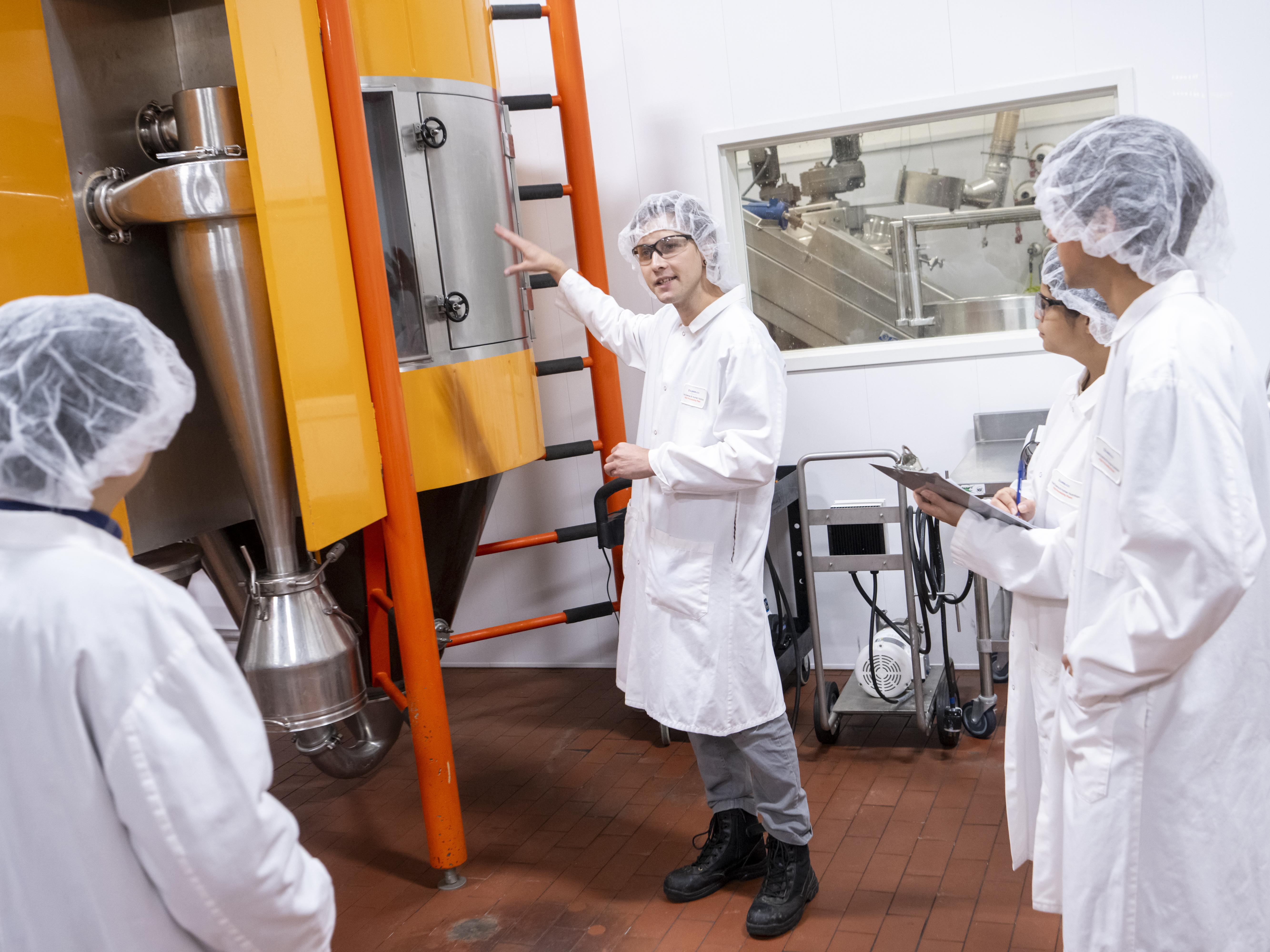 Three students in lab coats and hairnets.